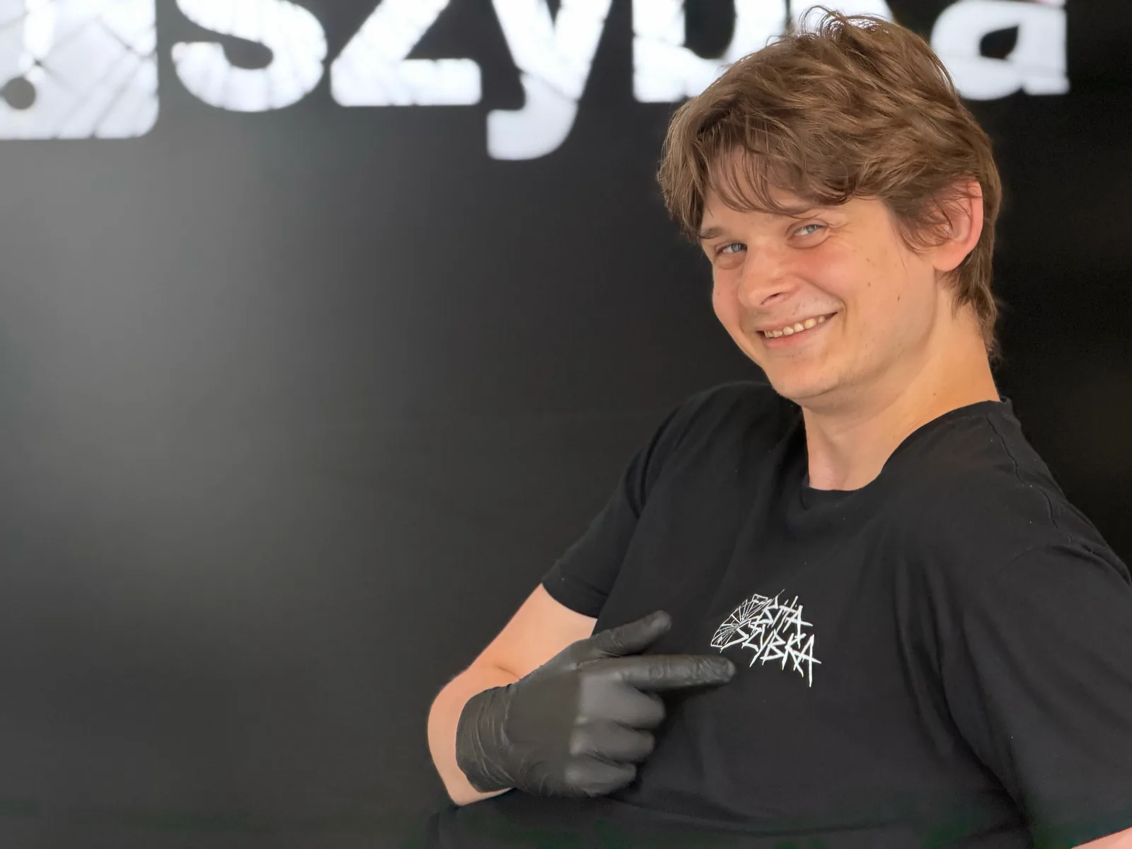 Uśmiechnięty serwisant w koszulce ZbitaSzybka wskazujący na logo