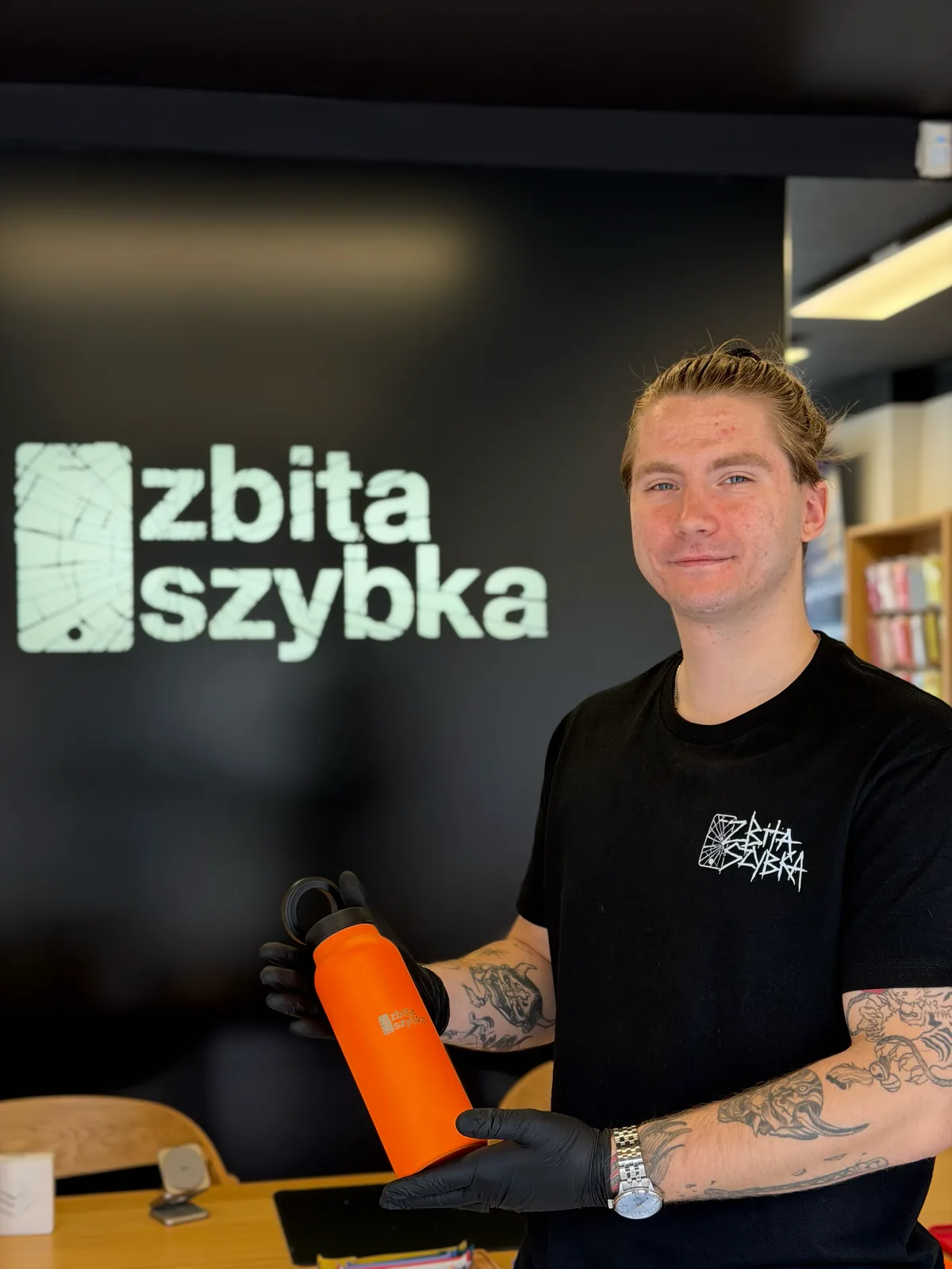 Pracownik ZbitaSzybka z butelką termiczną na tle logo