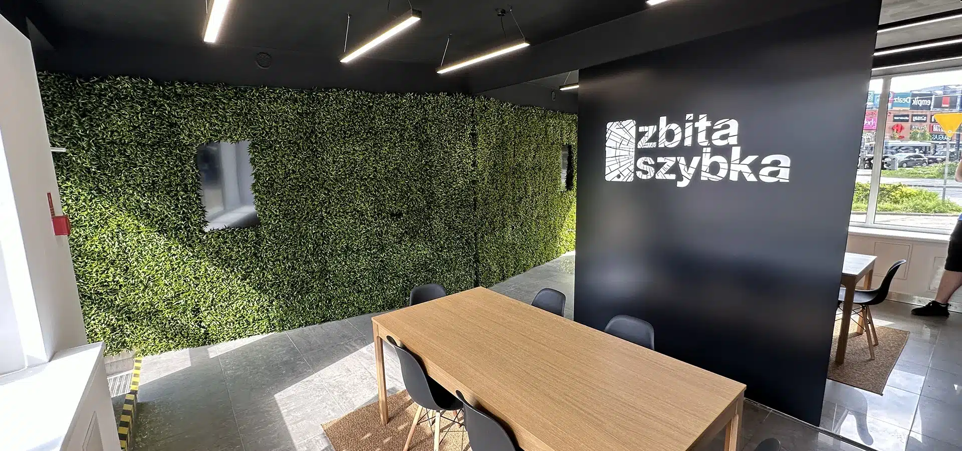 Wnętrze salonu ZbitaSzybka w Olsztynie ze stołem i ścianą porośniętą zielenią